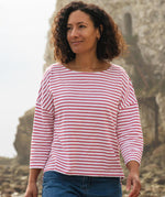 A woman standing outside wearing the Rapanui striped boat neck t-shirt in redwood stripe design. A organic cotton long sleeve top in a relaxed fit style with white and red stripes