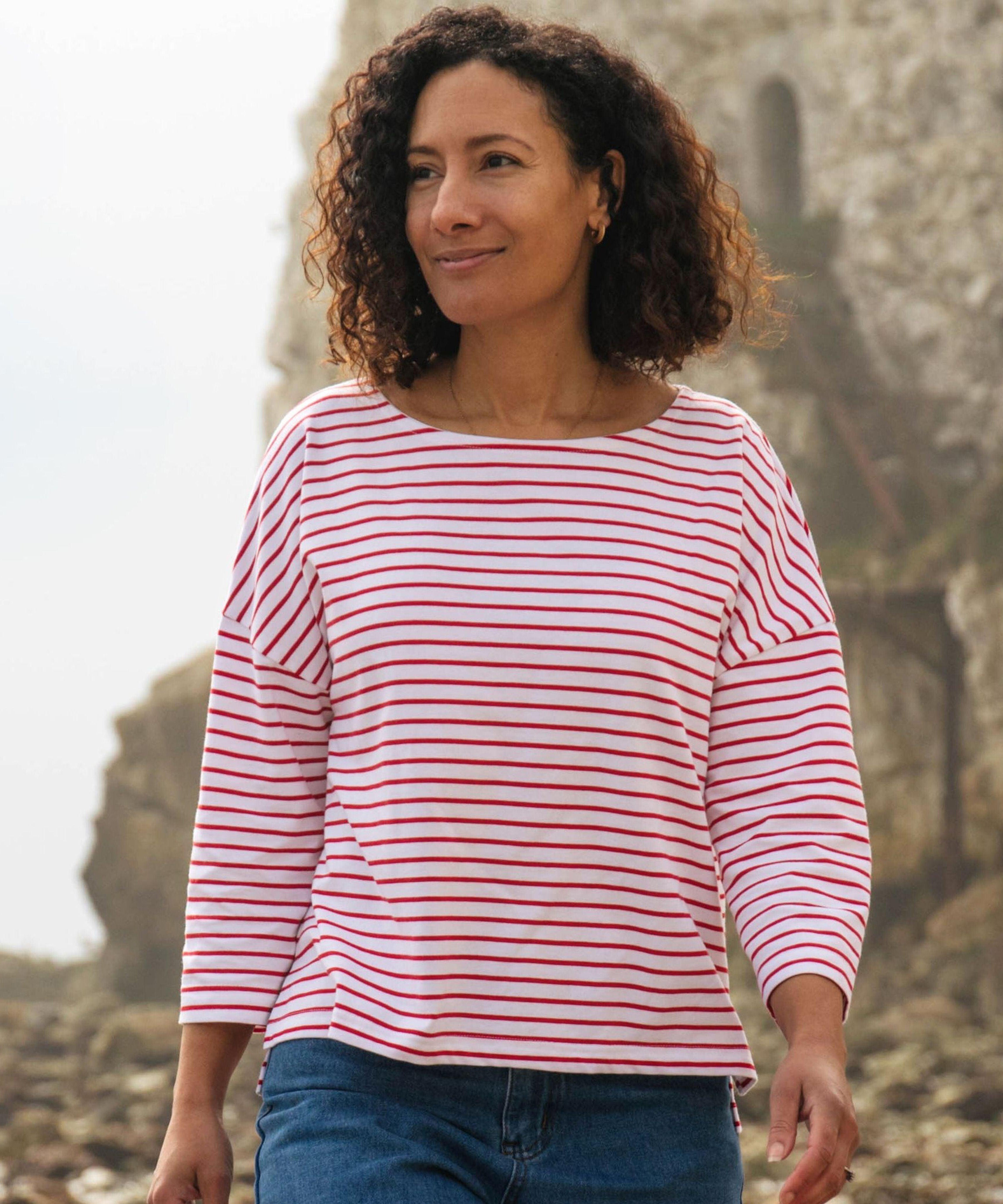 A woman standing outside wearing the Rapanui striped boat neck t-shirt in redwood stripe design. A organic cotton long sleeve top in a relaxed fit style with white and red stripes