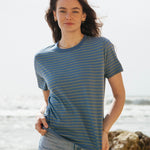 A woman standing outside wearing the Rapanui striped t-shirt. A organic cotton long sleeve top in a relaxed fit style with blue and sage stripes and blue neck trim