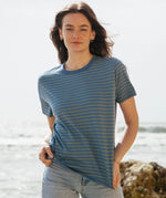 A woman standing outside wearing the Rapanui striped t-shirt. A organic cotton long sleeve top in a relaxed fit style with blue and sage stripes and blue neck trim