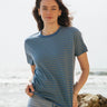 A woman standing outside wearing the Rapanui striped t-shirt. A organic cotton long sleeve top in a relaxed fit style with blue and sage stripes and blue neck trim