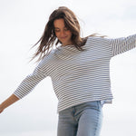 A woman standing outside wearing the Rapanui striped boat neck t-shirt in solent stripe design. A relaxed fit style organic cotton long sleeve top with a blue and white stripe design