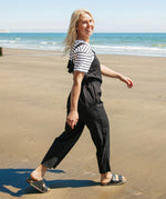 A woman walking on the beach wearing the black Rapanui organic cotton jumpsuit and striped top. 