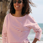 A woman standing outside wearing the Rapanui striped boat neck t-shirt in redwood stripe design. A organic cotton long sleeve top in a relaxed fit style with white and red stripes