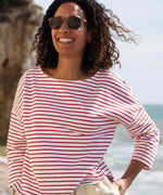 A woman standing outside wearing the Rapanui striped boat neck t-shirt in redwood stripe design. A organic cotton long sleeve top in a relaxed fit style with white and red stripes