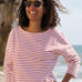 A woman standing outside wearing the Rapanui striped boat neck t-shirt in redwood stripe design. A organic cotton long sleeve top in a relaxed fit style with white and red stripes