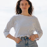 A woman standing outside wearing the Rapanui striped boat neck t-shirt in solent stripe design. A organic cotton long sleeve top in a relaxed fit style. 