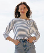 A woman standing outside wearing the Rapanui striped boat neck t-shirt in solent stripe design. A organic cotton long sleeve top in a relaxed fit style. 