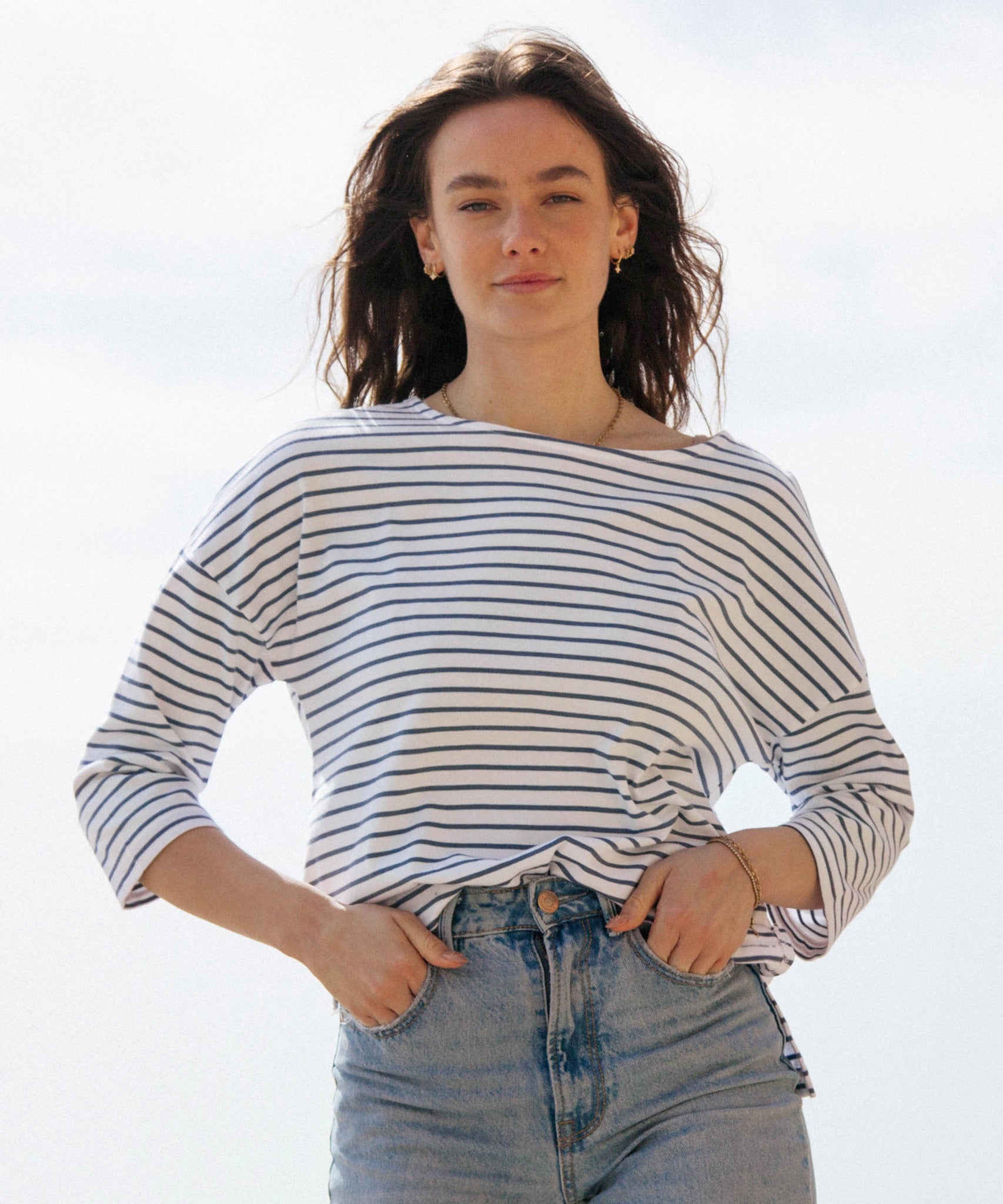 A woman standing outside wearing the Rapanui striped boat neck t-shirt in solent stripe design. A organic cotton long sleeve top in a relaxed fit style. 