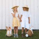stood next to a fence outside. The child is holding the handle of the Olli Ella Rattan Bunny Luggy with Lining – Pansy Floral. A beautifully woven pull along Luggy basket with cream cotton lining with a vintage pa