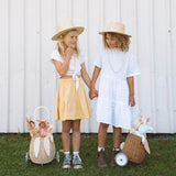stood next to a fence outside. The child is holding the handle of the Olli Ella Rattan Bunny Luggy with Lining – Pansy Floral. A beautifully woven pull along Luggy basket with cream cotton lining with a vintage pa