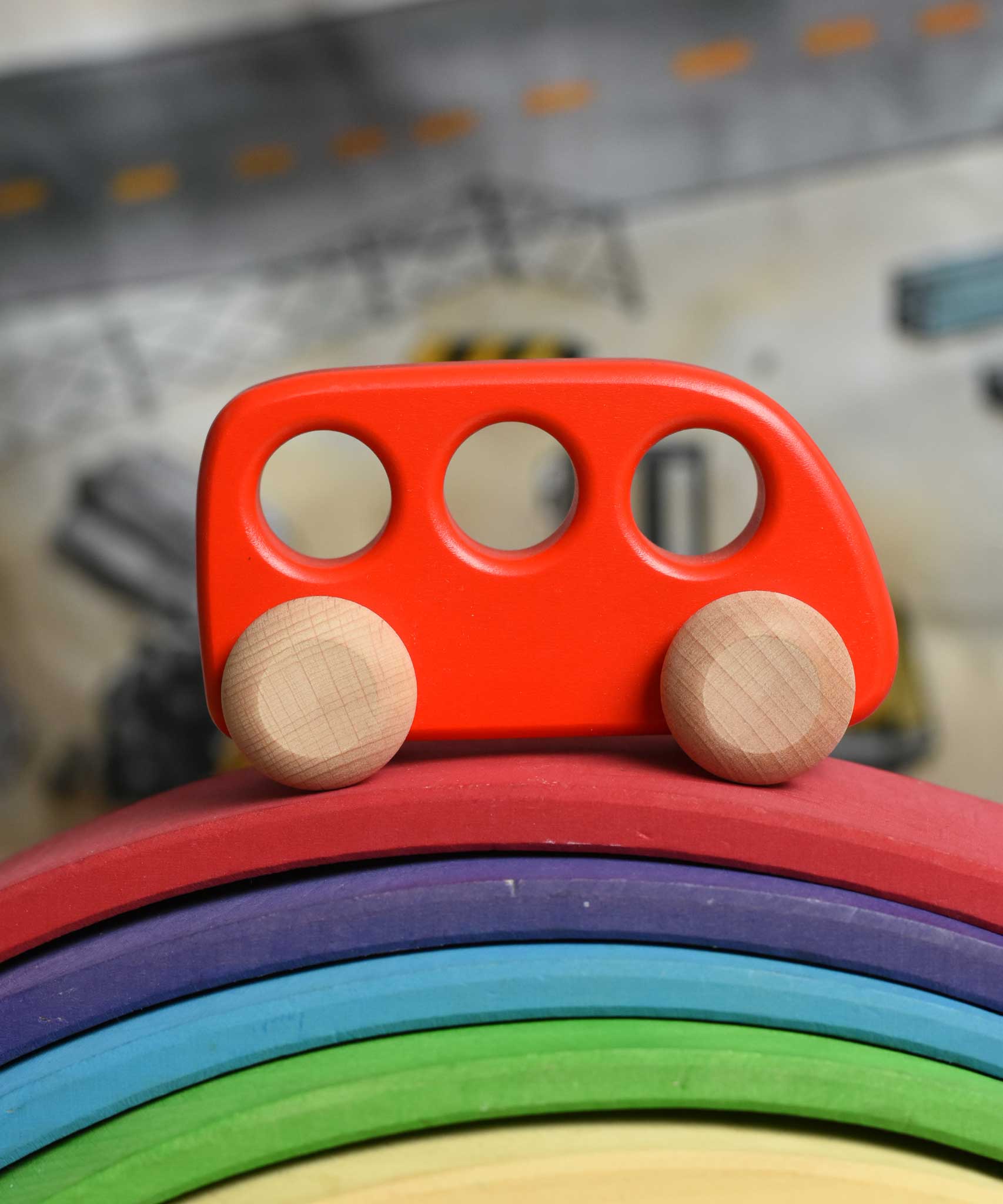 A red coloured Bajo bus wooden push along toy placed on a Gluckskafer bridge. These heirloom quality toys by Bajo are part of a wide range of wooden toys available here at Babipur. 