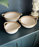 A set of 3 Respiin jute handled bowls in white and natural on top of a wooden dresser. 