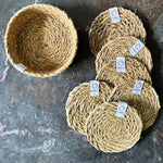 A top down view of the 6 Respiin seagrass coasters in natural with a matching holder on top of a stone surface Features a brand patch stitched on the rim.