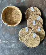 A top down view of the 6 Respiin seagrass coasters in natural with a matching holder on top of a stone surface Features a brand patch stitched on the rim.