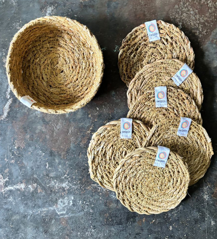 A top down view of the 6 Respiin seagrass coasters in natural with a matching holder on top of a stone surface Features a brand patch stitched on the rim.