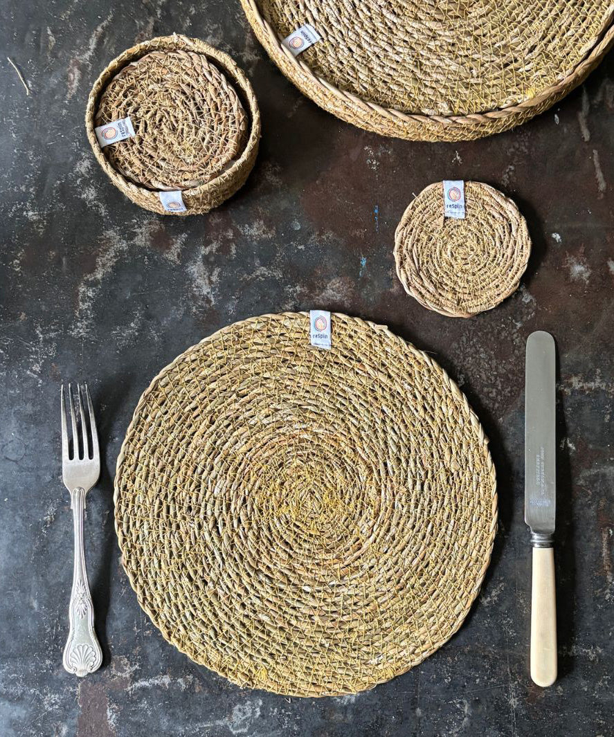 A top down view of the Respiin seagrass tablemat next to matching coasters on top of a stone surface next to a matching coasters 