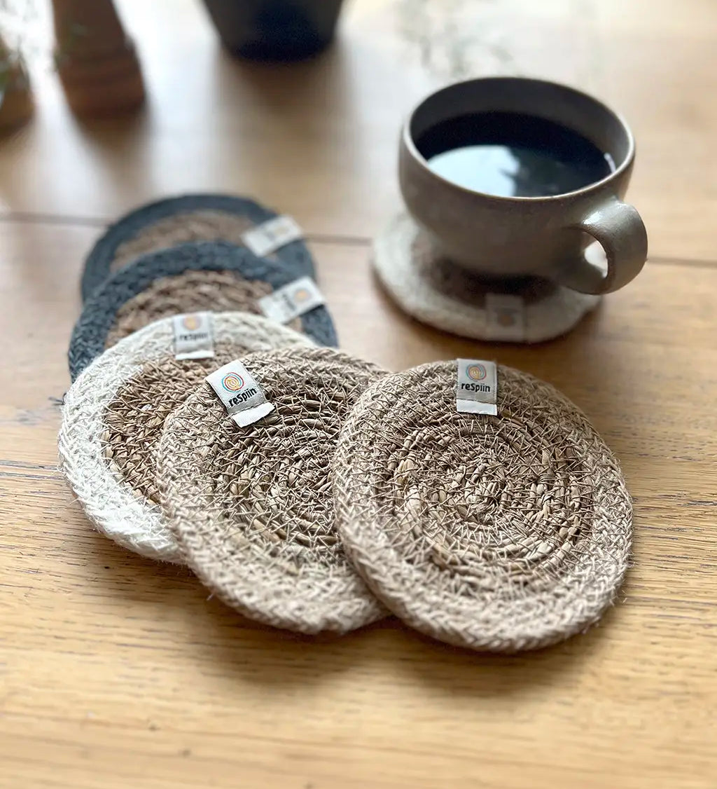 Set of 6 ReSpiin natural jute coasters on  a wooden table with a cup of coffee standing on one coaster