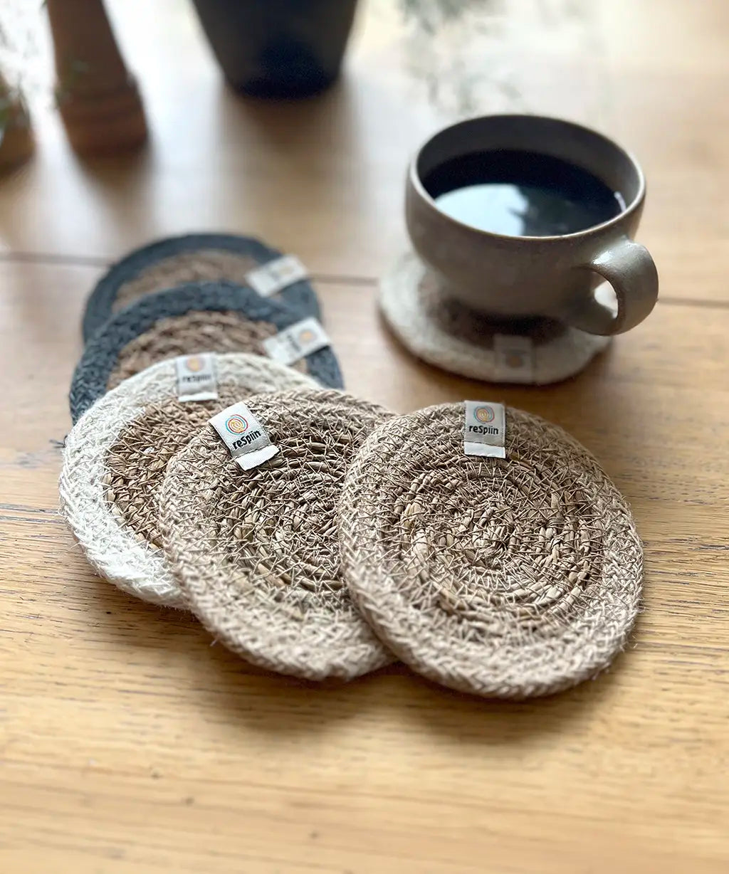 Set of 6 ReSpiin natural jute coasters on  a wooden table with a cup of coffee standing on one coaster