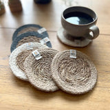 Set of 6 ReSpiin natural jute coasters on  a wooden table with a cup of coffee standing on one coaster