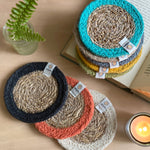 The ReSpiin natural jute and seagrass coasters on a table next to a book and a candle.