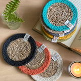 The ReSpiin natural jute and seagrass coasters on a table next to a book and a candle.