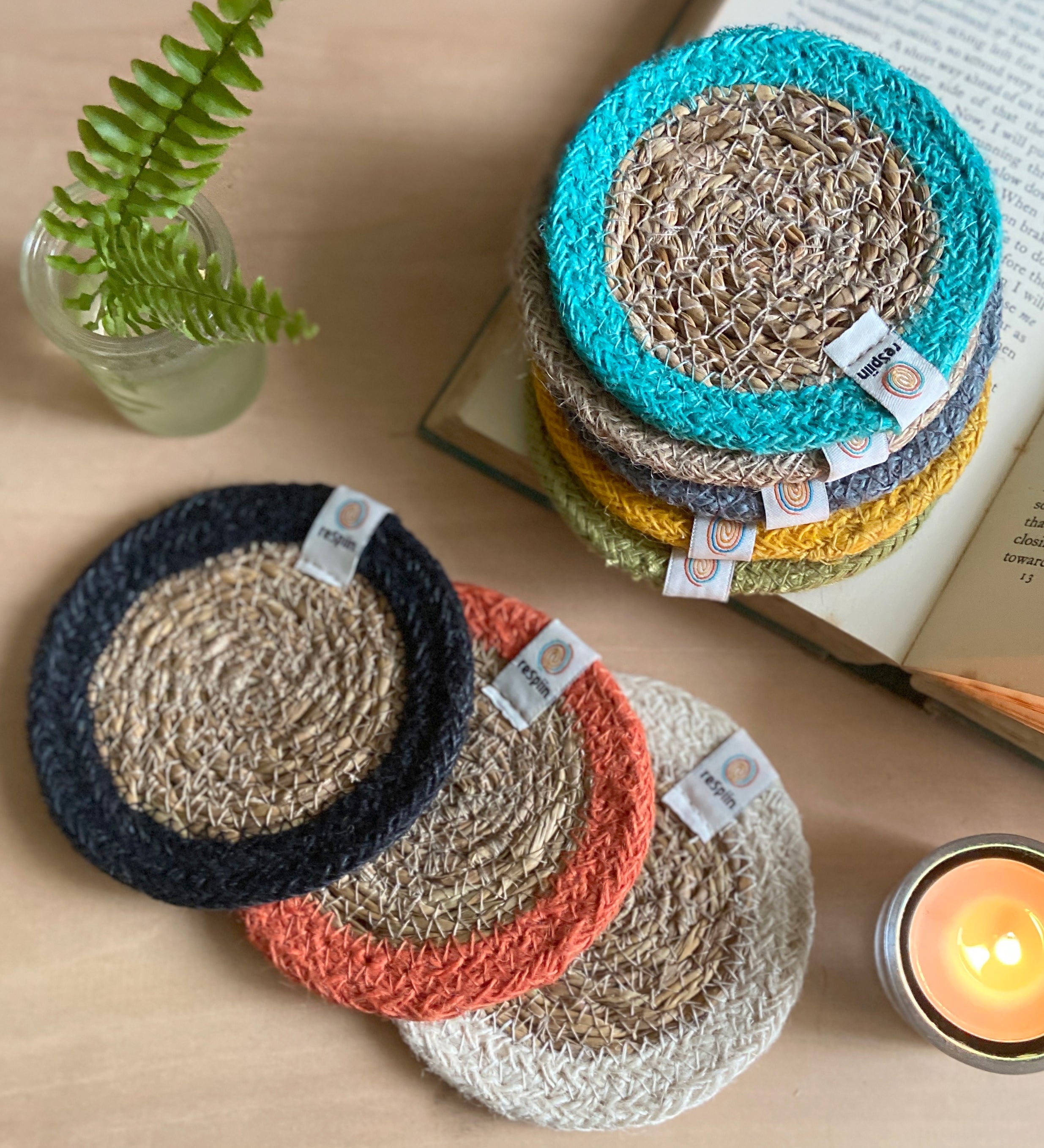 The ReSpiin natural jute and seagrass coasters on a table next to a book and a candle.