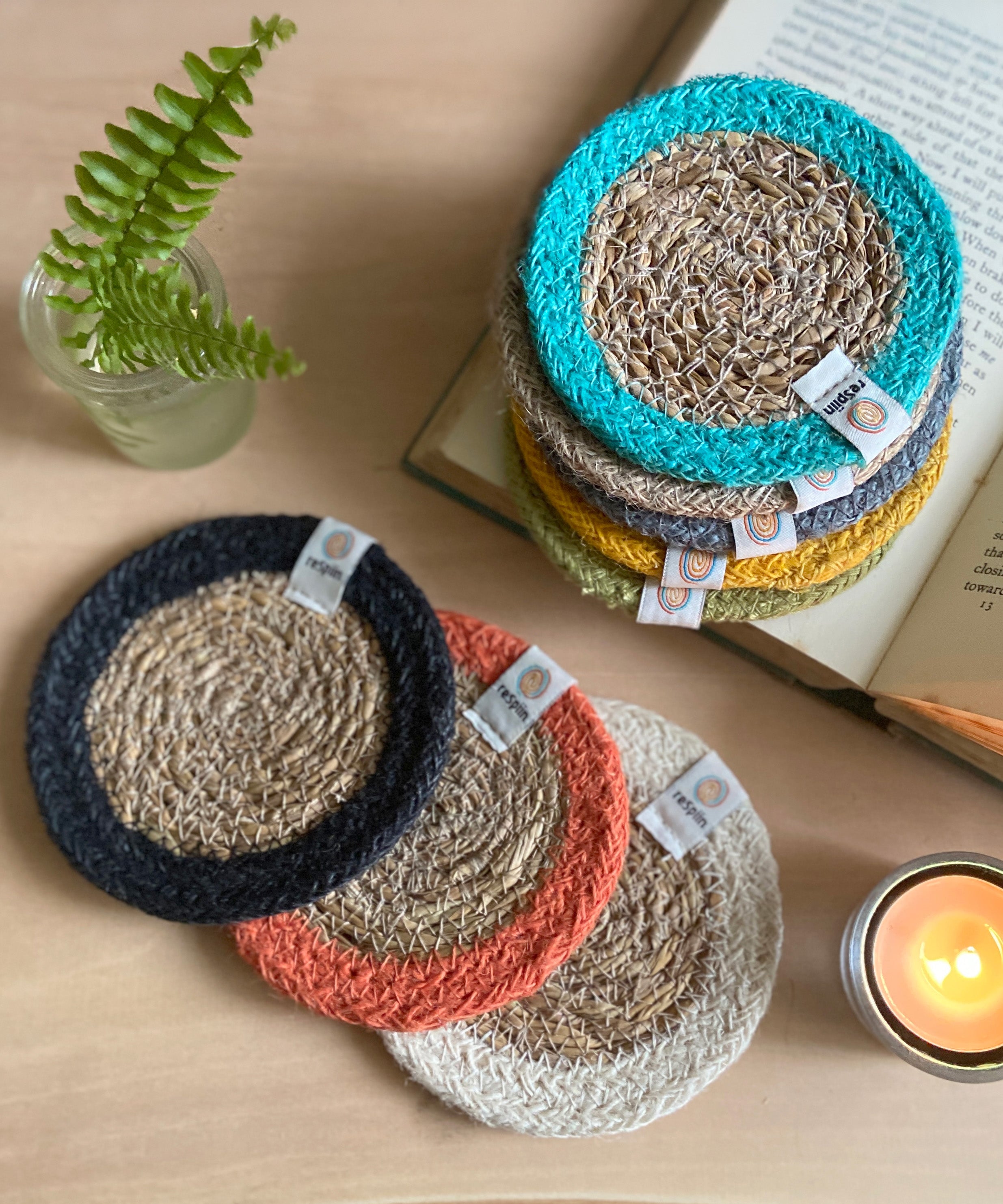 The ReSpiin natural jute and seagrass coasters on a table next to a book and a candle.