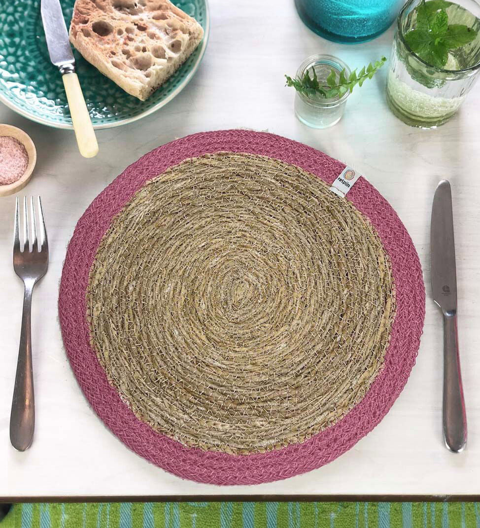The ReSpiin jute and seagrass handmade table mat in pink, laid on a set table.