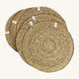A set of 6 Respiin seagrass tablemat in natural with a matching holder. Features a brand patch stitched on the rim.