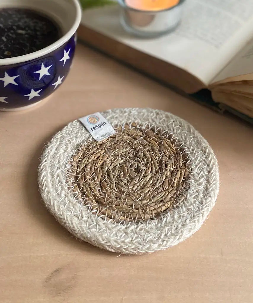 ReSpiin natural jute coaster with white rim on a table next to a book and cup of coffee