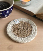 ReSpiin natural jute coaster with white rim on a table next to a book and cup of coffee
