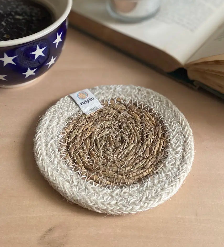 ReSpiin natural jute coaster with white rim on a table next to a book and cup of coffee