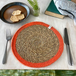 The ReSpiin seagrass and jute natural tablemat with an orange coloured ring, laid on a table.