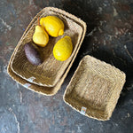 A top down view of the Respiin rectangular seagrass baskets on top of a stone surface with fruit inside the middle sized basket