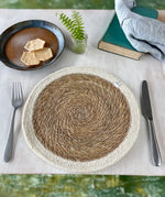 A Respiin jute table mat with white rim from the natural set on a table in between a knife and fork  