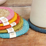 ReSpiin woven jute coasters stacked on a table showing a light blue, green, orange yellow, pink rim
