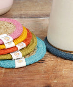 ReSpiin woven jute coasters stacked on a table showing a light blue, green, orange yellow, pink rim