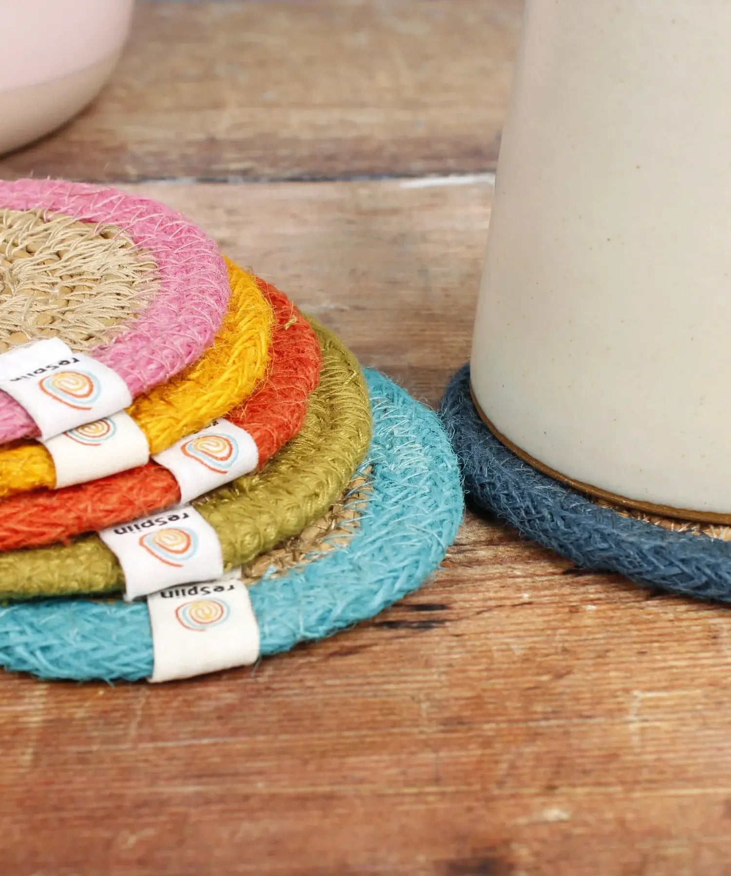 ReSpiin woven jute coasters stacked on a table showing a light blue, green, orange yellow, pink rim