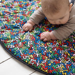 A baby lying down and looking at the 'Baby' print on the Etta Loves X Keith Haring Reversible Organic Cotton Baby Play Mat
