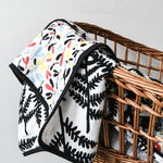 A child cuddling up to the Etta Loves Reversible Organic Cotton Muslin Blanket - Plant Print with black and white Ferns on one side