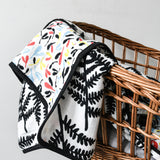 A child cuddling up to the Etta Loves Reversible Organic Cotton Muslin Blanket - Plant Print with black and white Ferns on one side