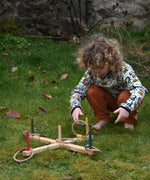 A child kneeling, playing with the Wooden Story Ring Toss Game. One of the hoops can be see mid-throw about to land on the base.