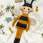 The Roommate Bee Rag Doll laying on a patterned duvet cover. 