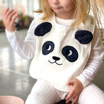 Child sat on a grey kitchen worktop wearing the Roommate Panda Baby Bib in organic cotton with embroidered panda face with 3D ears. She has a bowl of blueberries beside her.