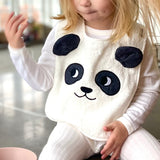 Child sat on a grey kitchen worktop wearing the Roommate Panda Baby Bib in organic cotton with embroidered panda face with 3D ears. She has a bowl of blueberries beside her.