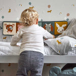 A child standing in front of a bed with the Roommate Country Life Fabric Book tied to the side.