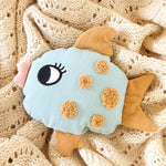 A Roommate Fish Rattle on a cream coloured knitted blanket. 