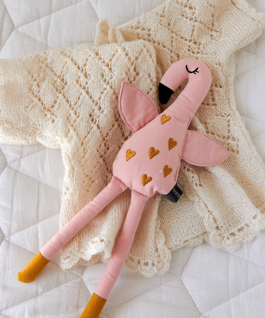 A Roommate Flamingo Rag Doll placed on a cream coloured knitted cardigan.