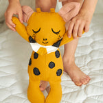 A child holding the Roommate Canvas Doll Goldy The Giraffe up in a standing position by it's arms. 
